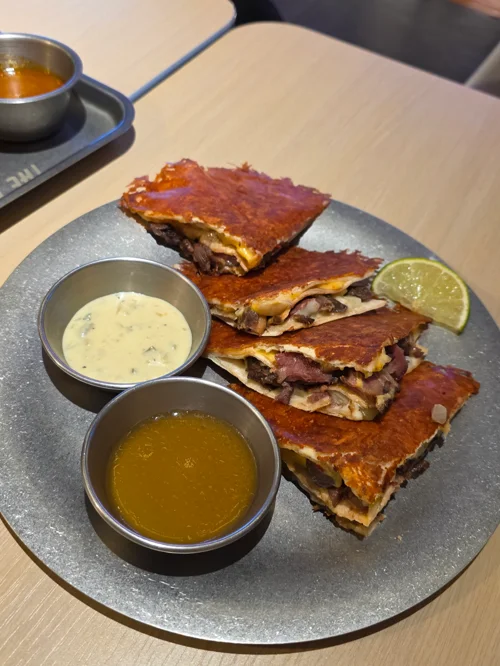 네 조각으로 잘린 퀘사디아와 소스 두 개, 라임이 놓인 검은 접시