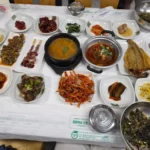 테이블 위에 된장찌개와 다양한 반찬들이 가득 차려진 한식 백반 상차림