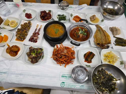테이블 위에 된장찌개와 다양한 반찬들이 가득 차려진 한식 백반 상차림
