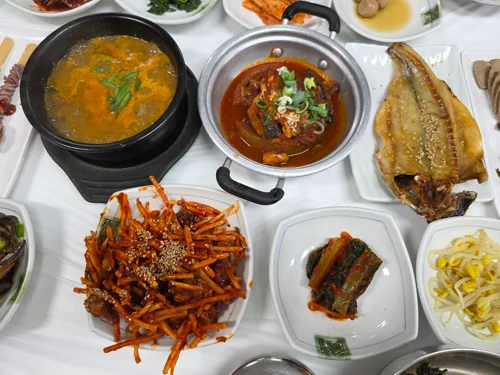 뚝배기 찌개, 오징어볶음, 생선구이와 다양한 밑반찬이 차려진 한식 정식 상차림