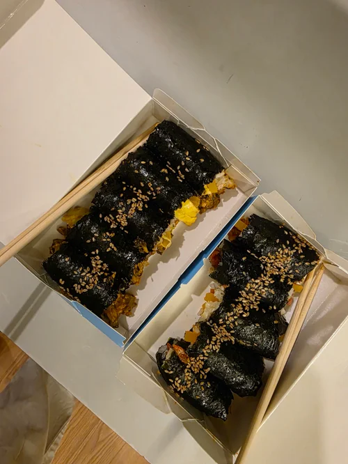 깨가 뿌려진 김밥 두 줄이 투명 플라스틱 용기에 담긴 모습