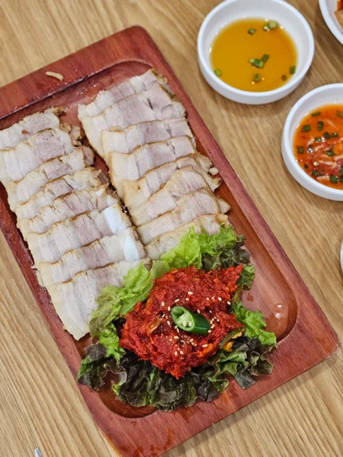 나무 플래터에 담긴 얇게 썬 보쌈 수육과 상추, 양념장