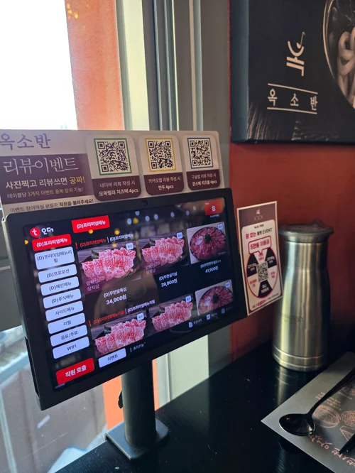고깃집 테이블에 설치된 디지털 주문 키오스크 화면에 다양한 고기 메뉴가 표시된 모습