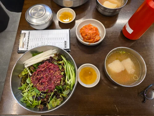 육회와 채소가 올라간 비빔밥과 무국, 김치가 차려진 한식 세트 메뉴