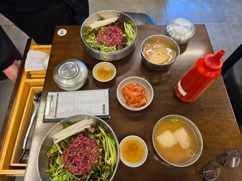 나무 트레이 위 육회비빔밥 2인분과 반찬, 무국이 세팅된 식탁