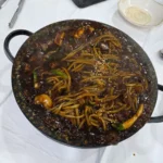 검은 철판에 담긴 짜장면, 춘장 소스와 채소 고명이 올려진 모습