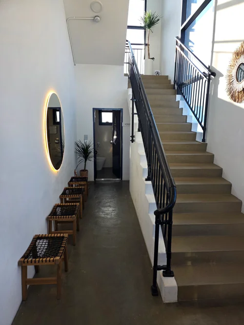 타원형 LED 거울과 라탄 벤치가 있는 모던한 화이트톤 실내 계단 공간