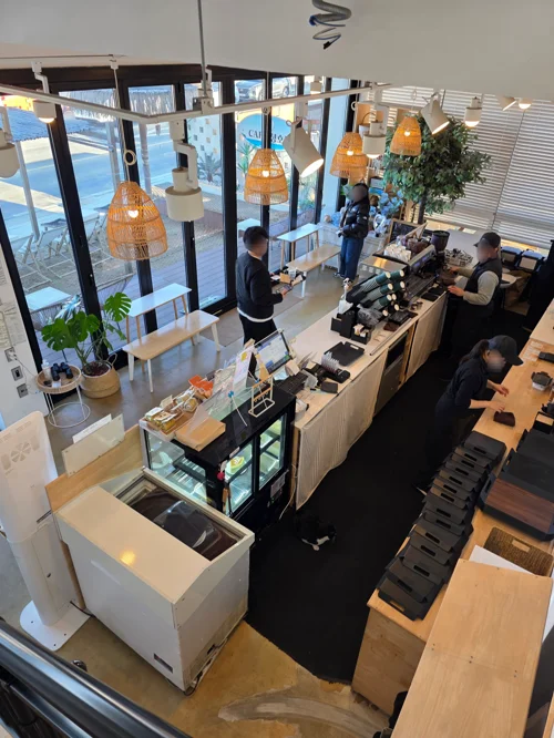 밝은 목재 카운터와 황토색 조명이 있는 모던 카페 내부 전경