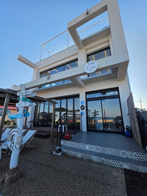 큰 유리창과 기하학적 디자인의 2층 화이트 건물, 해변가 카페 외관