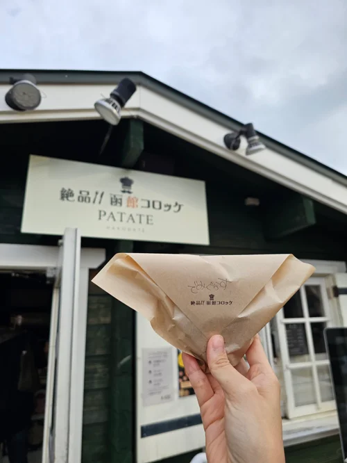 홋카이도 하코다테의 크로켓 전문점 PATATE 앞에서 포장지에 담긴 크로켓을 들고 있는 모습