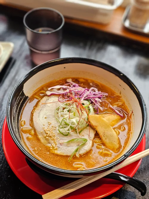 빨간 쟁반 위 검은 그릇에 담긴 차슈와 채소 토핑이 올라간 일본식 라멘