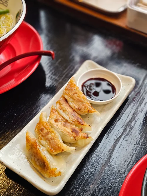 흰 접시에 담긴 노릇하게 구운 군만두 4조각과 간장 소스