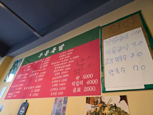 무등족발 메뉴판, 빨간 배경에 족발 보쌈 가격이 적혀있고 오른쪽에 점심메뉴 가격이 적힌 흰 종이가 붙어있다