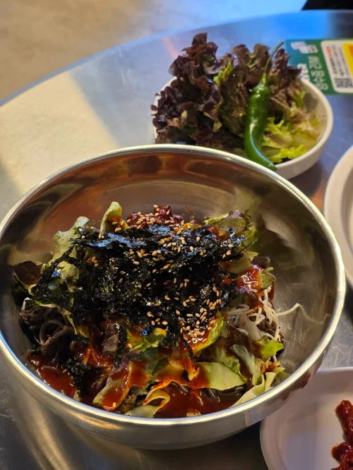 무등족발 서비스 비빔막국수, 스테인리스 그릇에 김가루와 참깨가 듬뿍 올라간 비빔막국수가 담겨있다