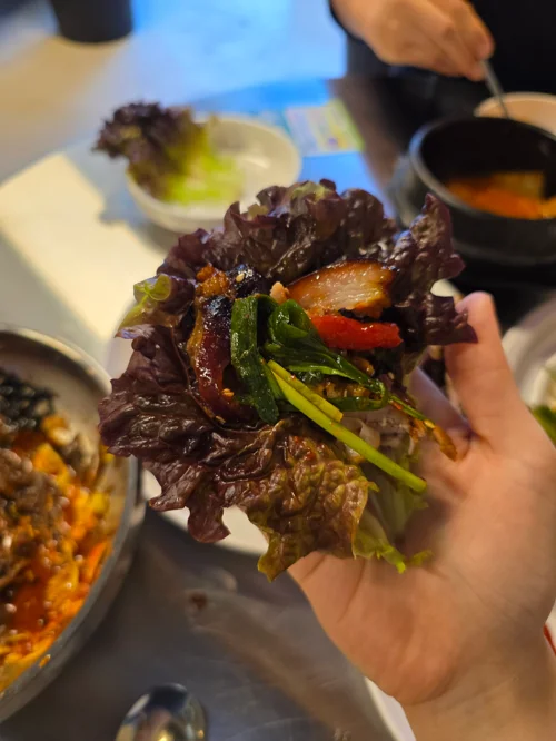 적상추에 족발과 부추 고추를 올려 쌈을 싸서 손에 들고 있는 모습