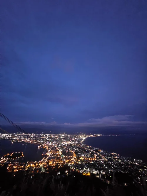 높은 곳에서 내려다본 해안 도시의 야경, 푸른 하늘과 반짝이는 불빛