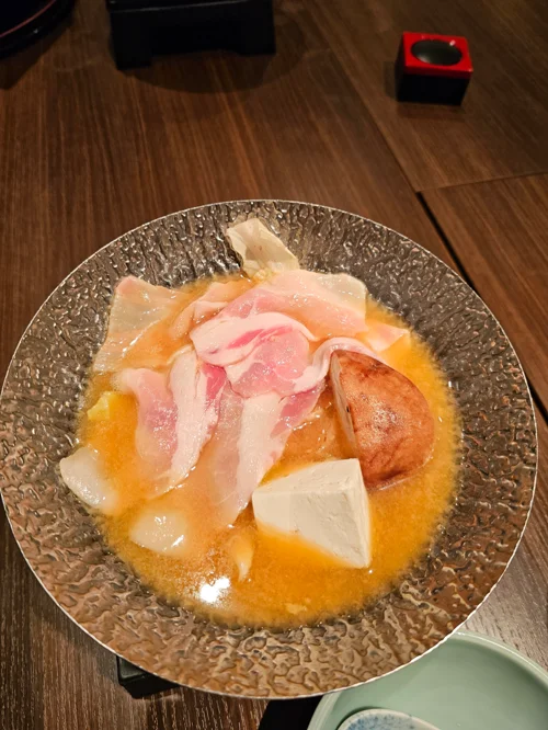 금속 냄비에 담긴 주황색 미소 국물의 돼지고기 두부 전골 요리