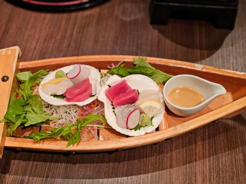 나무 보트 접시에 참치 회 세 점이 조개껍데기 위에 놓인 일식 플레이팅