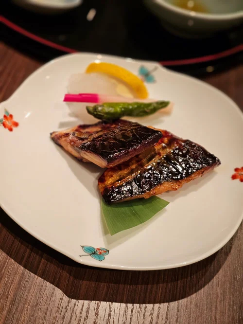 꽃무늬 흰 도자기 접시에 담긴 윤기 나는 간장 양념 생선 구이와 채소 곁들임