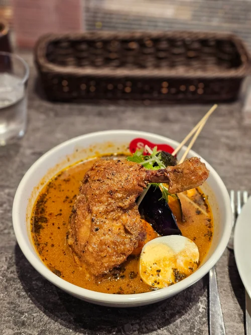 흰 그릇에 담긴 통닭다리와 가지 삶은 달걀이 들어간 스프 카레