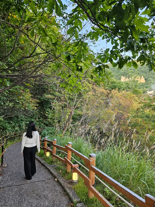 붉은 난간이 있는 숲속 산책로를 걷는 여성의 뒷모습
