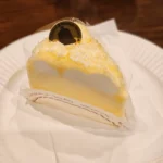 흰 접시 위에 놓인 레몬 크림 슬라이스 케이크, 금색 초콜릿 장식 포함