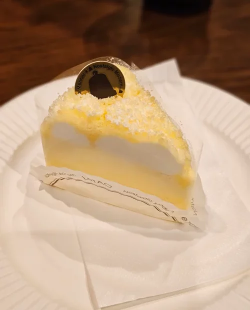 흰 접시 위에 놓인 레몬 크림 슬라이스 케이크, 금색 초콜릿 장식 포함