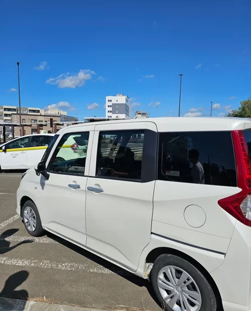 파란 하늘 아래 일본 주차장에 주차된 흰색 슬라이딩 도어 미니밴