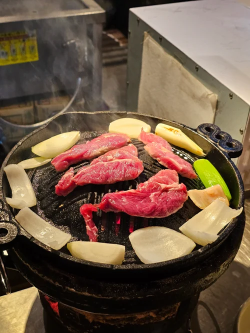 숯불 화로 그릴 위에 신선한 양고기와 양파, 마늘이 구워지고 있는 장면