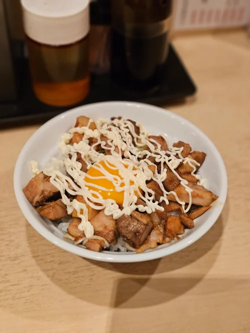 흰 그릇에 담긴 고기 덮밥 위에 달걀 노른자와 마요네즈가 올려진 모습