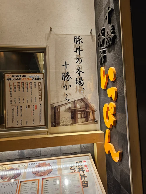 豚丼の本場 十勝から 포스터와 오렌지색 간판이 있는 일본 돈부리 전문점 입구