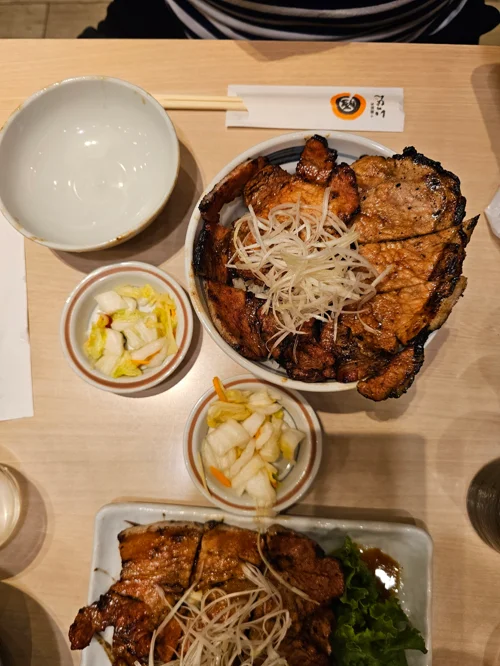 구운 돼지고기와 채 썬 파가 올려진 일본식 덮밥과 피클 반찬