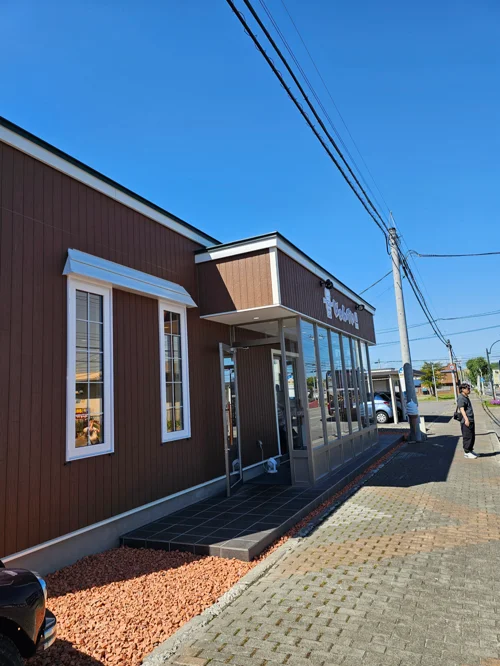 파란 하늘 아래 갈색 목조 외관과 유리 현관이 있는 카페 건물 외부 전경