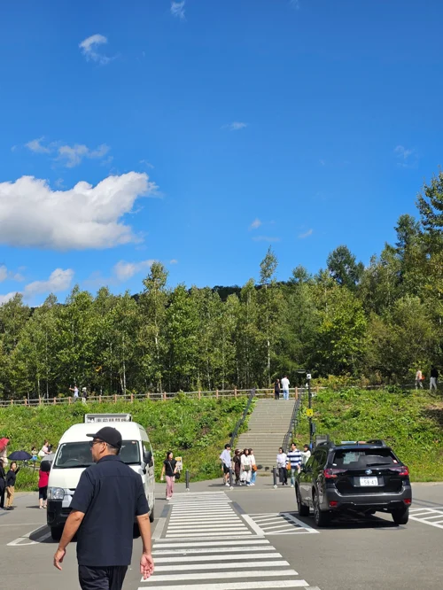 맑은 여름 하늘 아래 녹음이 우거진 언덕으로 이어지는 계단과 관광객들