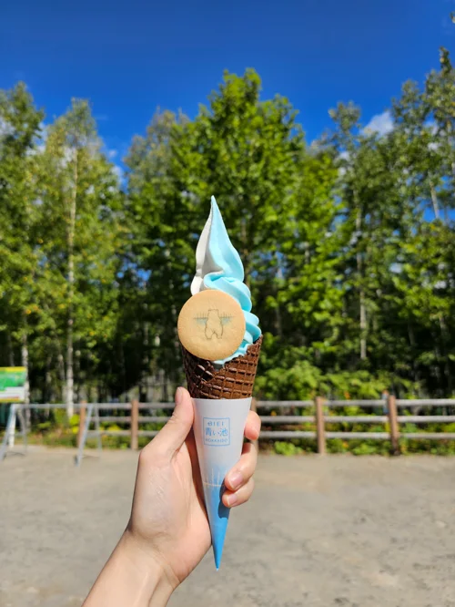 파란 하늘 아래 하늘색과 흰색 믹스 소프트아이스크림 콘을 손에 들고 있는 모습