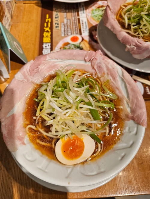 차슈로 그릇을 감싼 스파이시 라멘에 파, 콩나물, 반숙 계란이 토핑된 모습