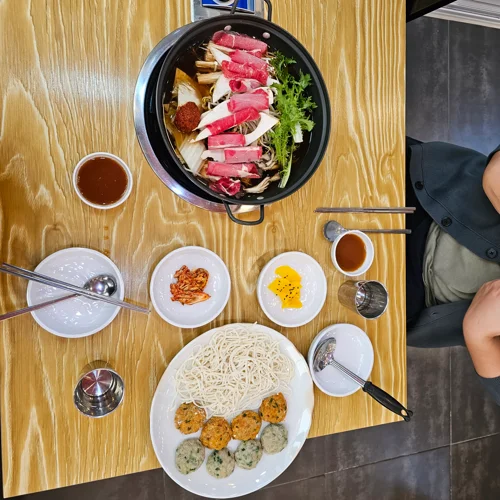 소고기 슬라이스와 채소가 담긴 전골 냄비와 소면, 어묵볼이 놓인 한식 상차림