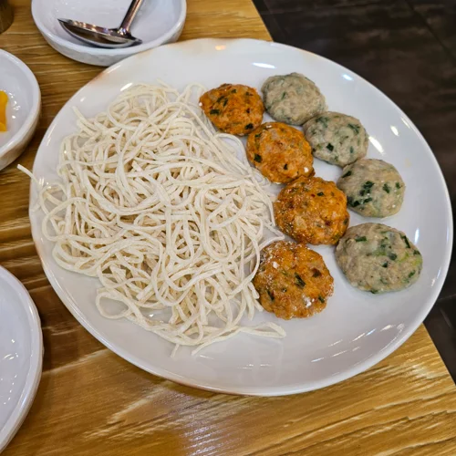 흰 접시에 쌀국수 면과 두 종류의 완자볼이 담긴 아시안 요리