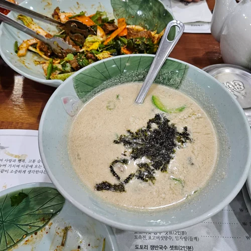 청자 그릇에 담긴 크리미한 도토리 쟁반국수, 김 가루와 애호박 고명 올림