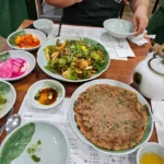 한식당 테이블에 녹색 채소 전과 나물 무침, 반찬들이 차려진 한 상 차림