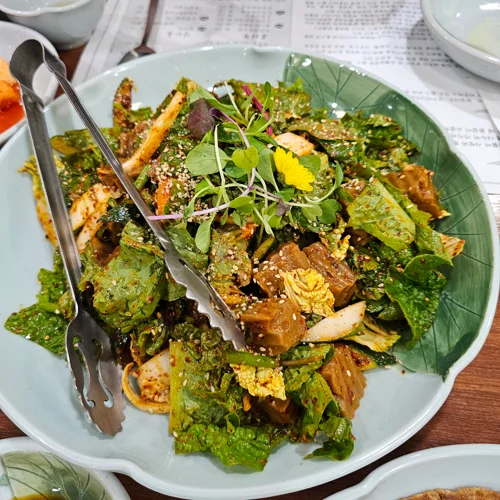 연잎 모양 접시에 담긴 두부와 쌈채소 샐러드에 식용 꽃과 새싹이 장식된 모습