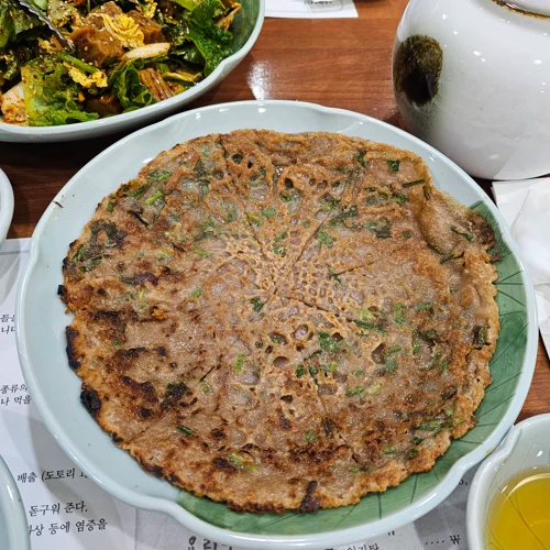 갈색으로 바삭하게 구워진 파전이 흰 접시에 담겨 있는 모습