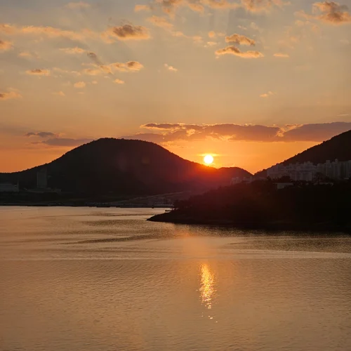 두 산 사이로 지는 주황빛 태양과 잔잔한 수면에 반사된 여수 노을