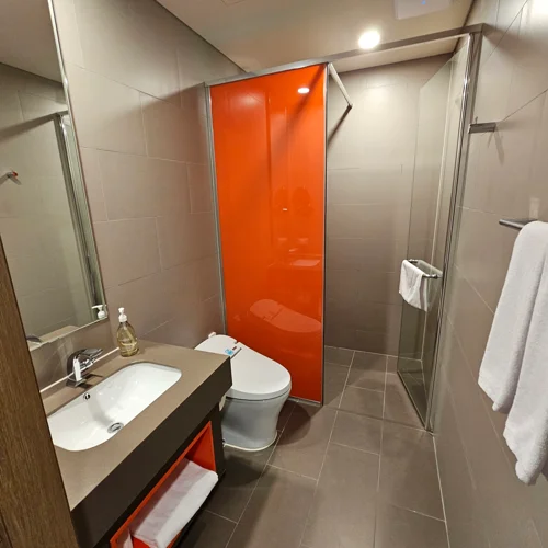 오렌지색 포인트 패널과 유리 샤워부스가 있는 여수 벨메르 호텔 욕실