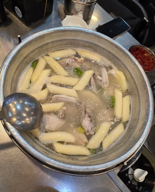 가스버너 위 냄비에 끓고 있는 닭고기와 떡이 담긴 뽀얀 국물 요리