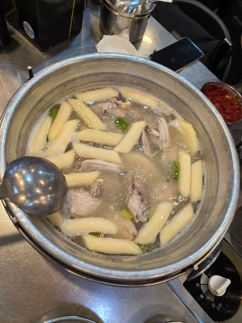 가스버너 위 냄비에 끓고 있는 닭고기와 떡이 담긴 뽀얀 국물 요리