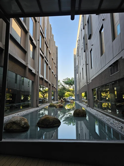 두 현대식 건물 사이 자연석이 놓인 잔잔한 수공간과 반영