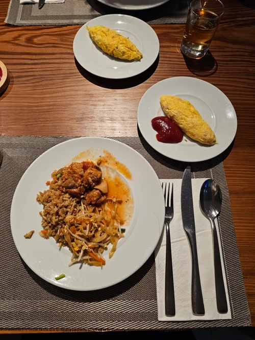 나무 테이블 위에 볶음밥과 오믈렛 두 개가 각각 흰 접시에 담긴 식사 장면