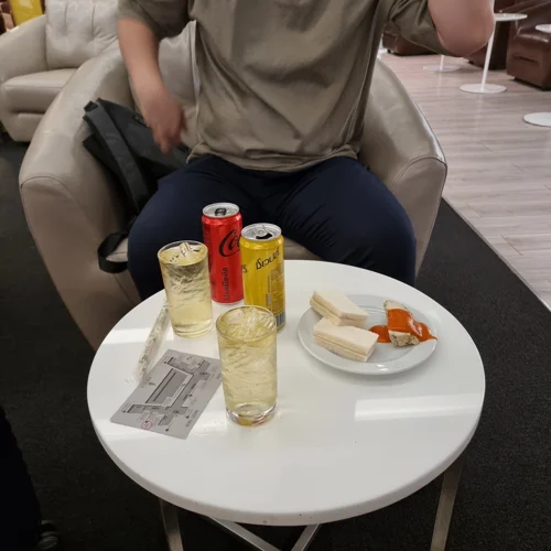 공항 라운지 테이블 위에 놓인 음료수 캔, 유리잔, 샌드위치 접시