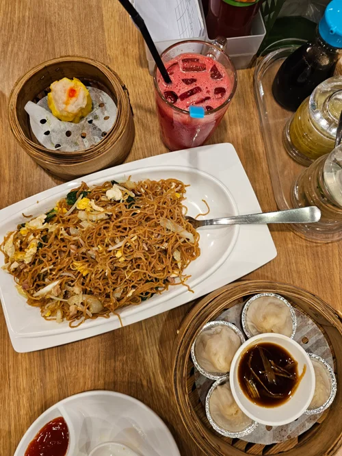 나무 테이블 위 볶음면 슈마이 만두 딤섬과 과일 주스가 차려진 중식 식사